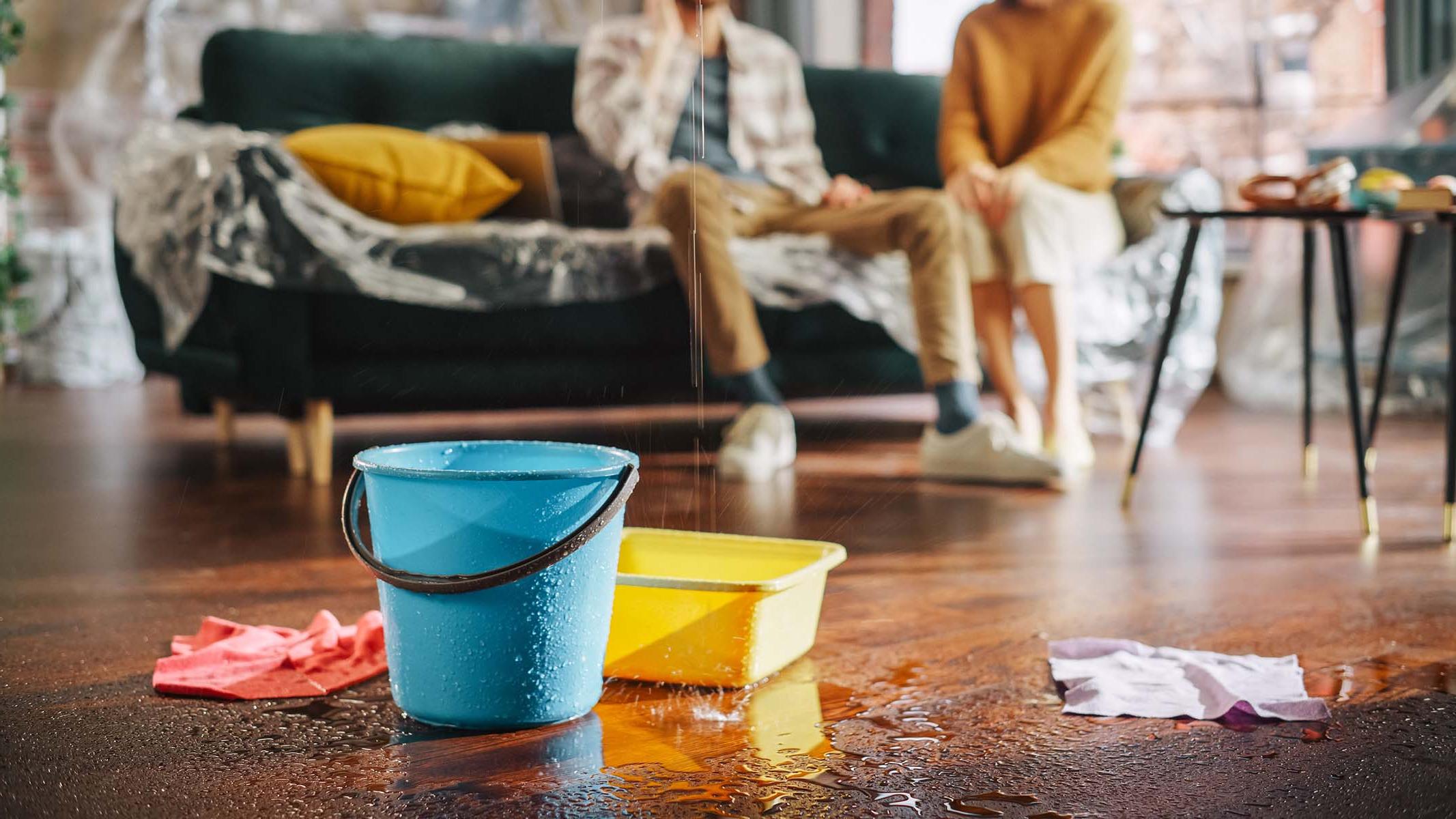 Buckets catch a leak on a wet floor with two people in the background.